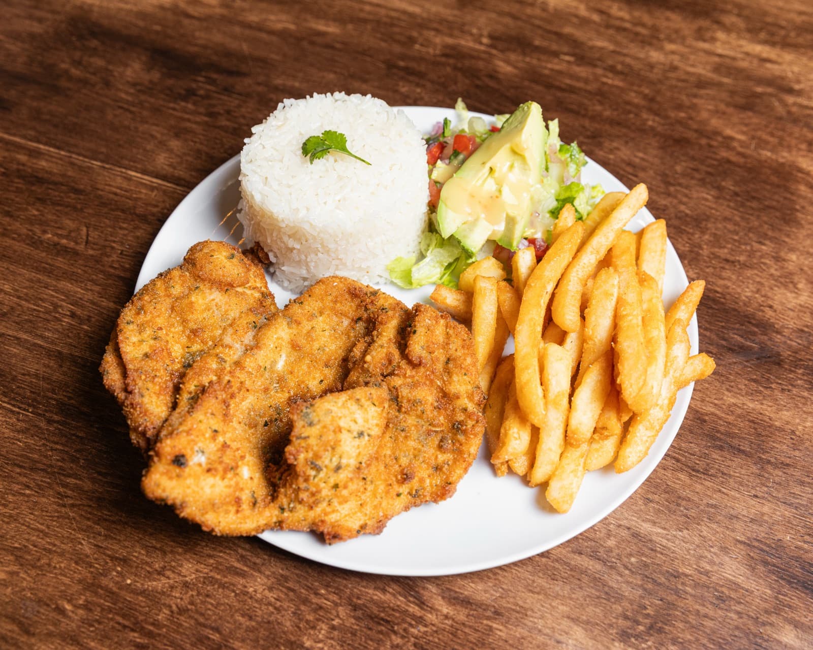 A plate of Lulada's milanesa — breaded fried chicken with rice, fries, and salad.