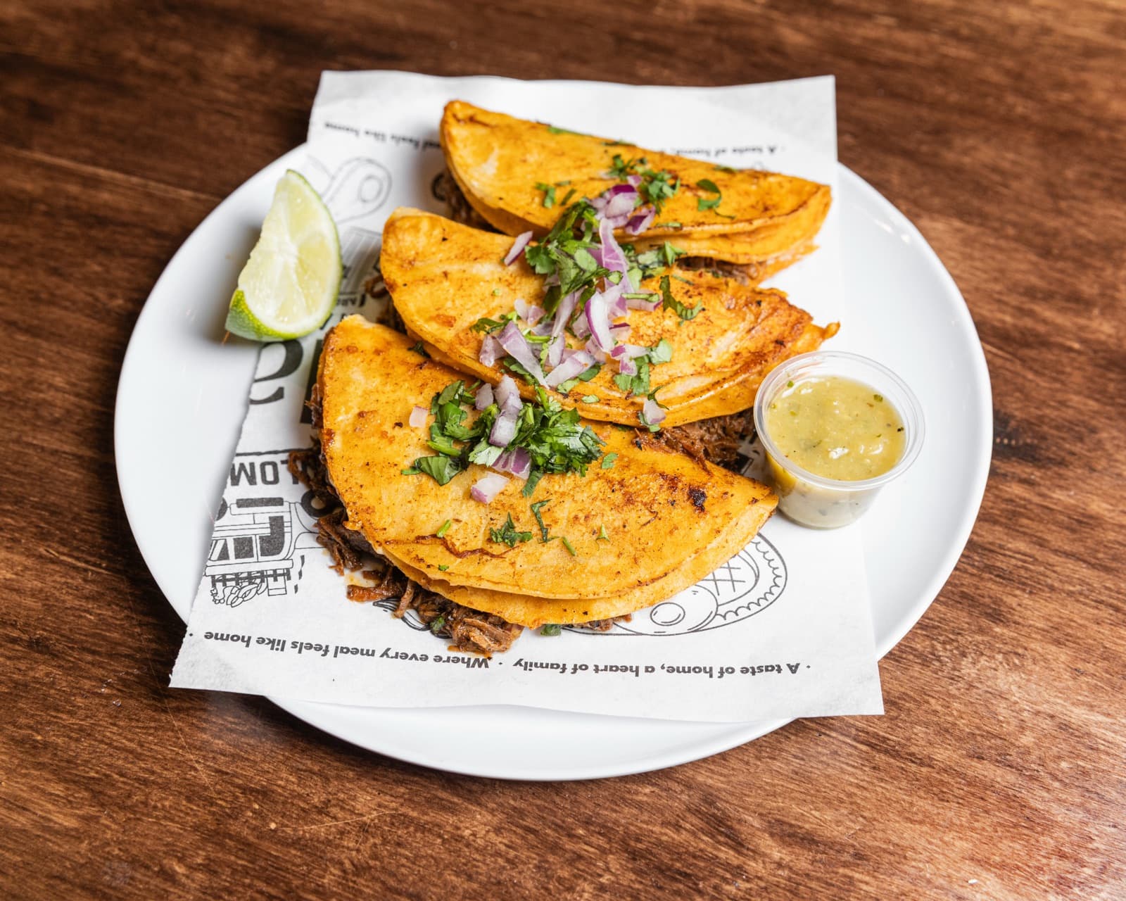 Cheesy birria quesabirria tacos with a lime wedge and consommé for dipping.